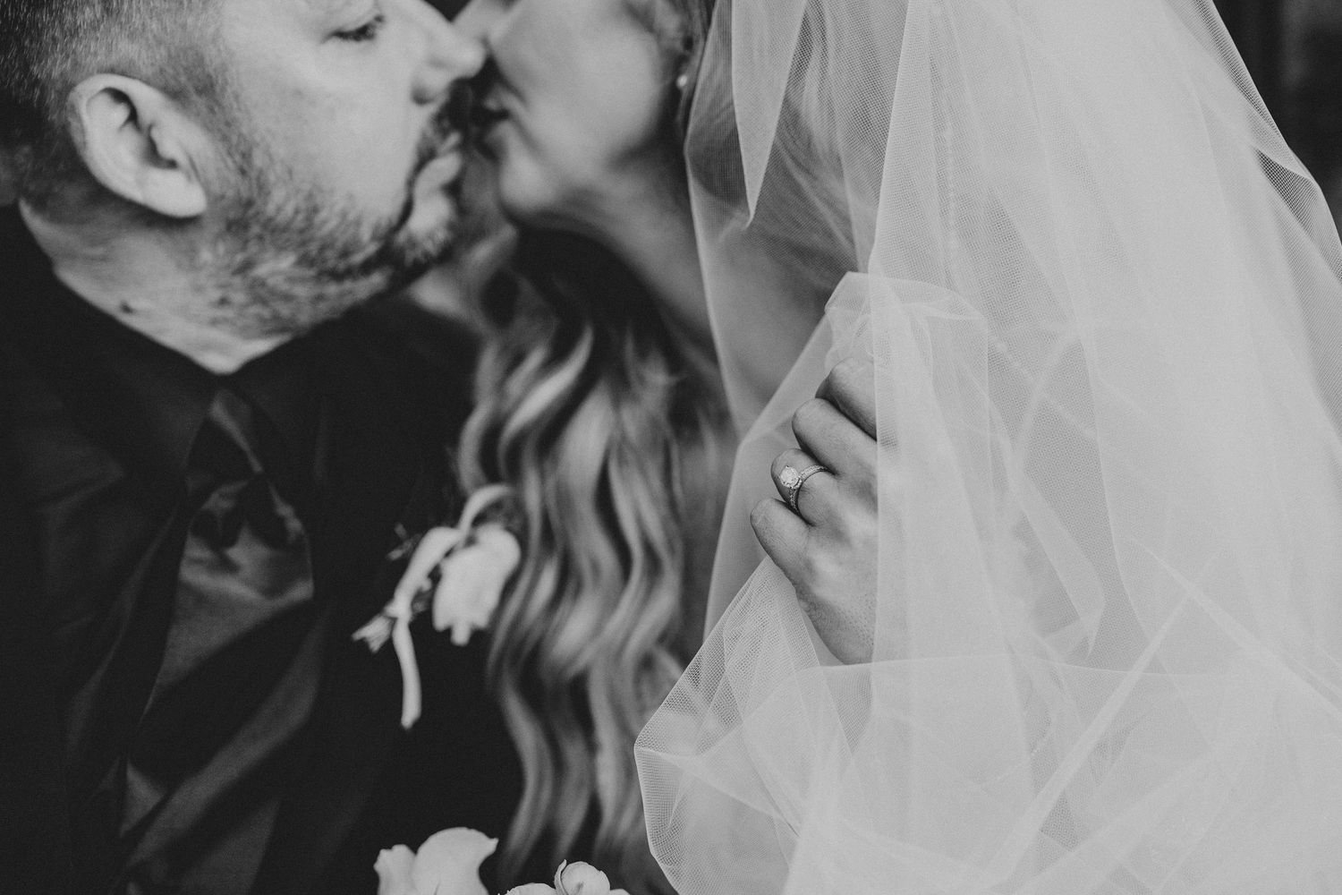Black and white photo of a bride and groom sharing a romantic kiss on their wedding day.