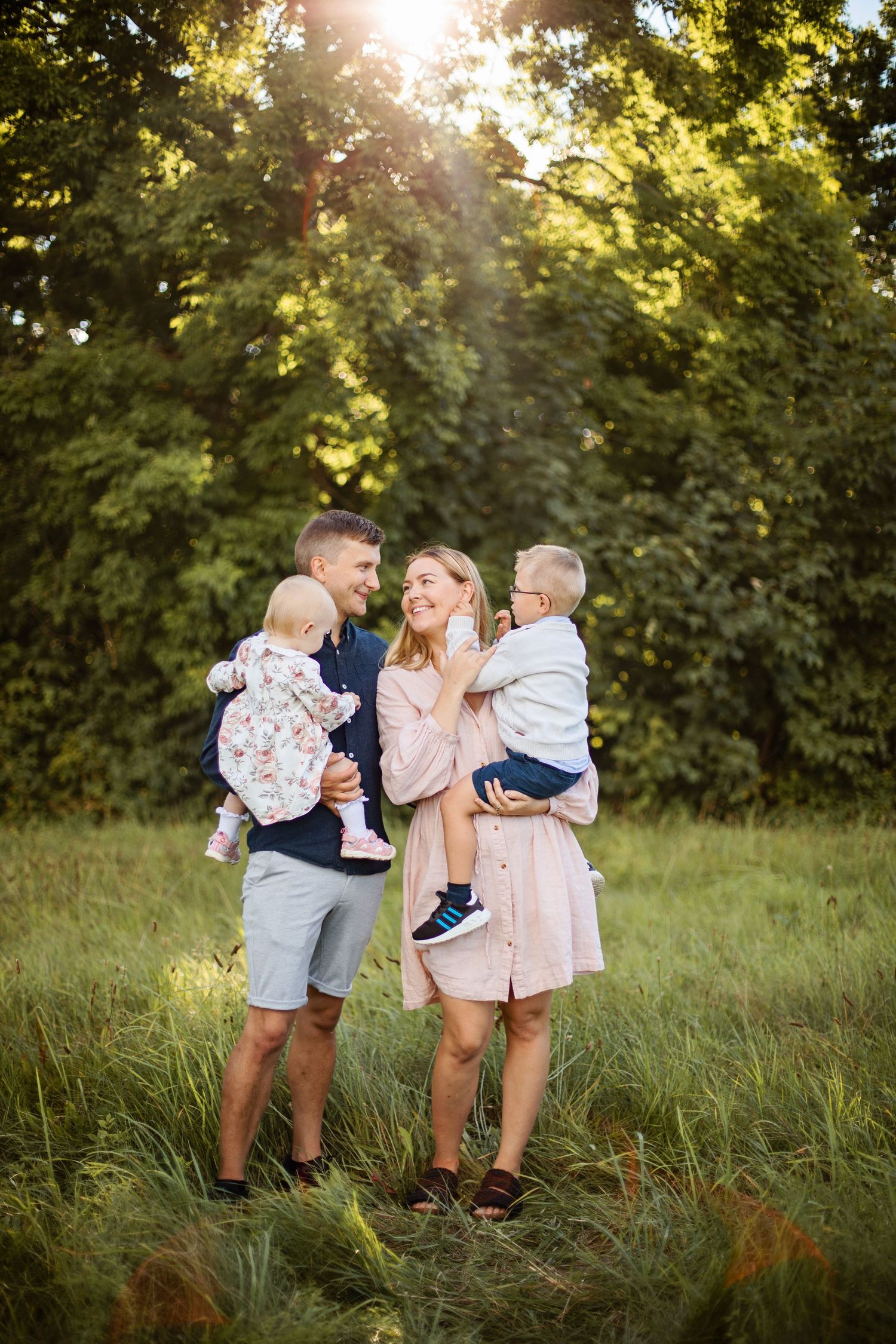 A family stands together in a sunlit meadow during golden hour with trees in the background.