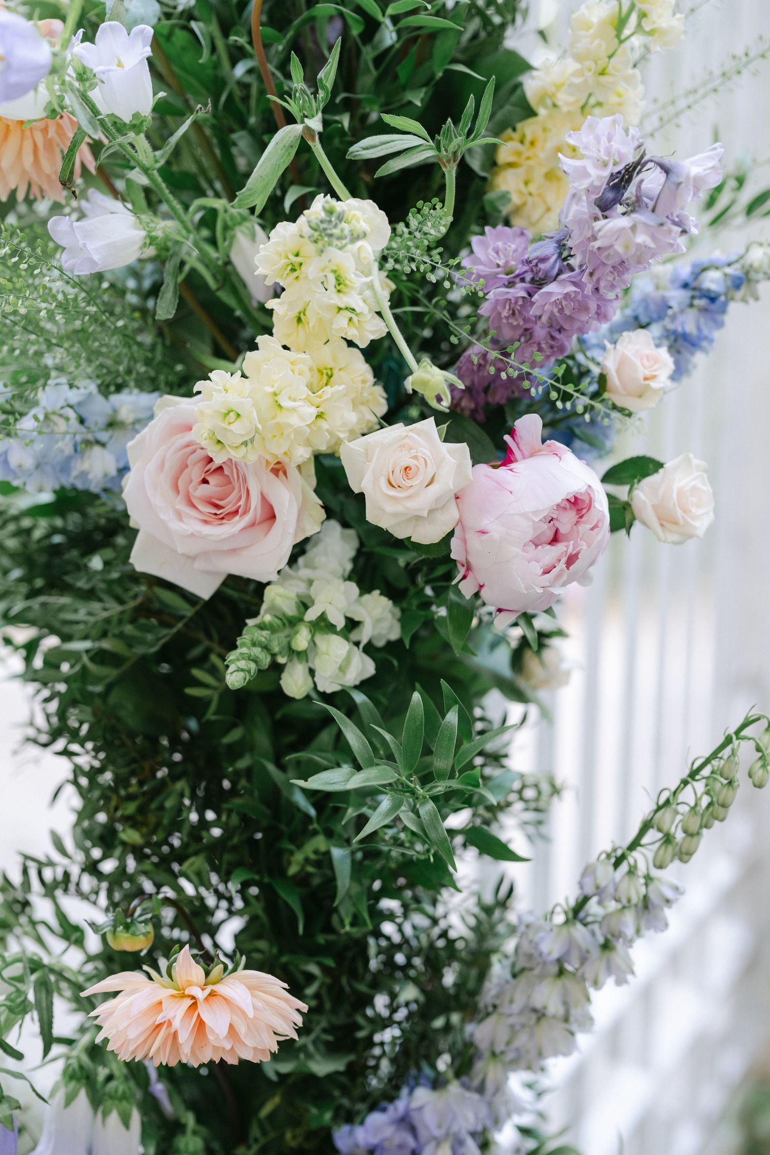 Lush floral arrangement with pink roses, peonies, lilac, and white blooms amid green foliage for a wedding decor display.