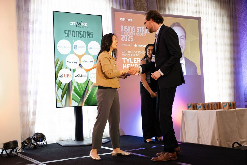 Two professionals shake hands on stage at the Rising Stars 2025 event with a sponsors backdrop.