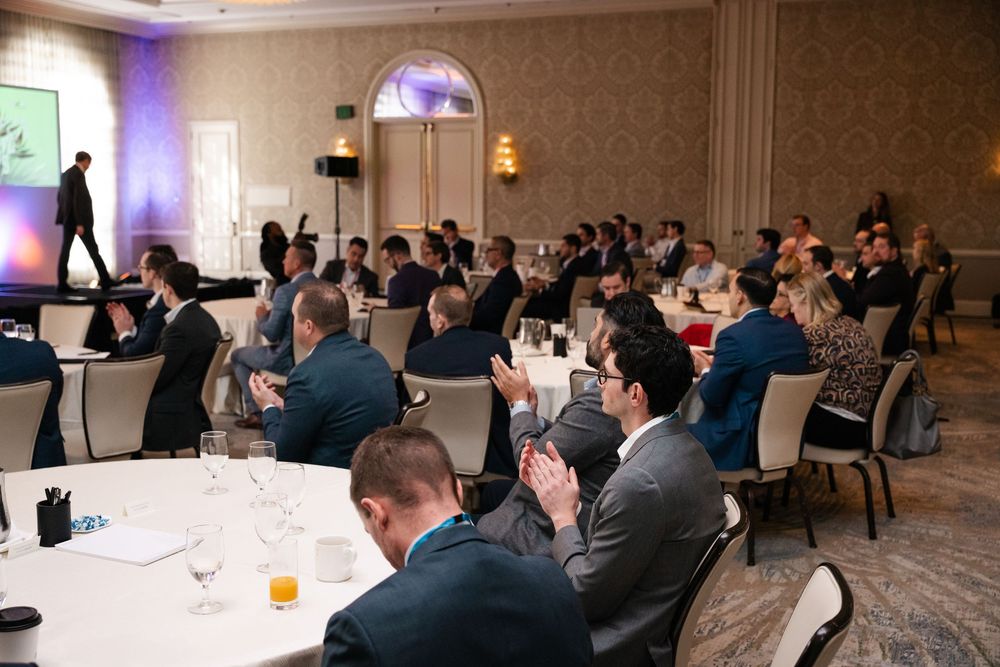 Business professionals in suits applaud a speaker at a corporate conference in an elegant hotel ballroom.