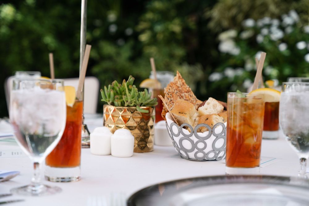 Outdoor party table with iced tea drinks, appetizers, and a succulent centerpiece on a white tablecloth.
