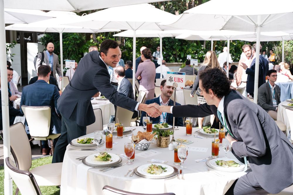 Business professionals shaking hands at an outdoor corporate luncheon with white tablecloths and elegant table settings.