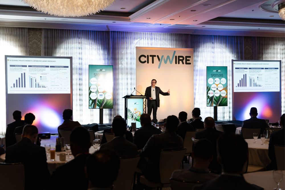 Speaker presents financial data on screens at a Citywire investment conference in a packed ballroom.