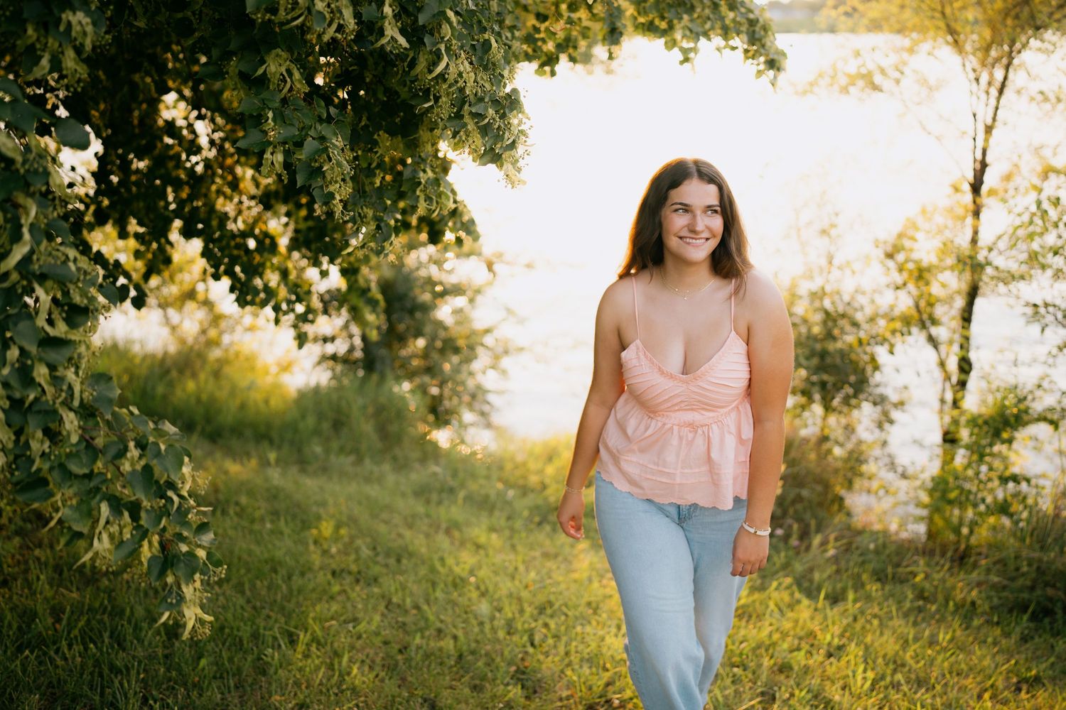 Young woman in pink top and jeans smiling while walking through a sunny wildflower meadow.
