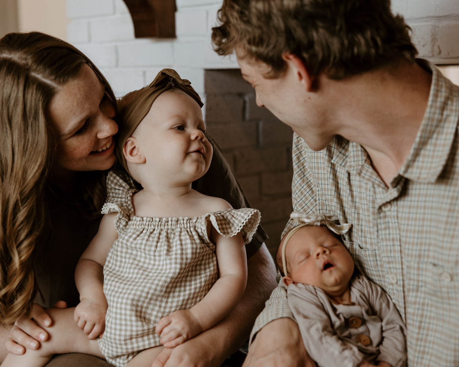 A happy young family with a toddler girl and newborn baby sharing a warm, tender moment together.