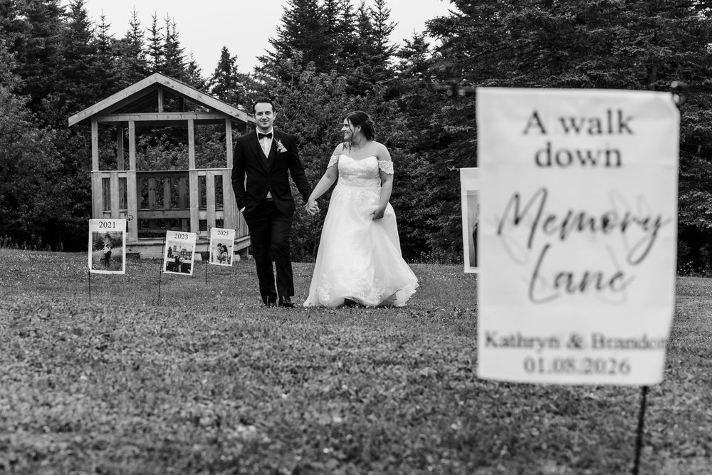 Black and white wedding photo of couple walking hand in hand past a Memory Lane sign at Kathryn & Brandon's wedding.
