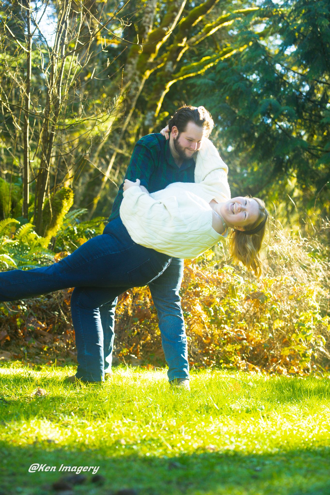 A man dips a laughing woman in a sunny green park during a romantic outdoor couples photo session.