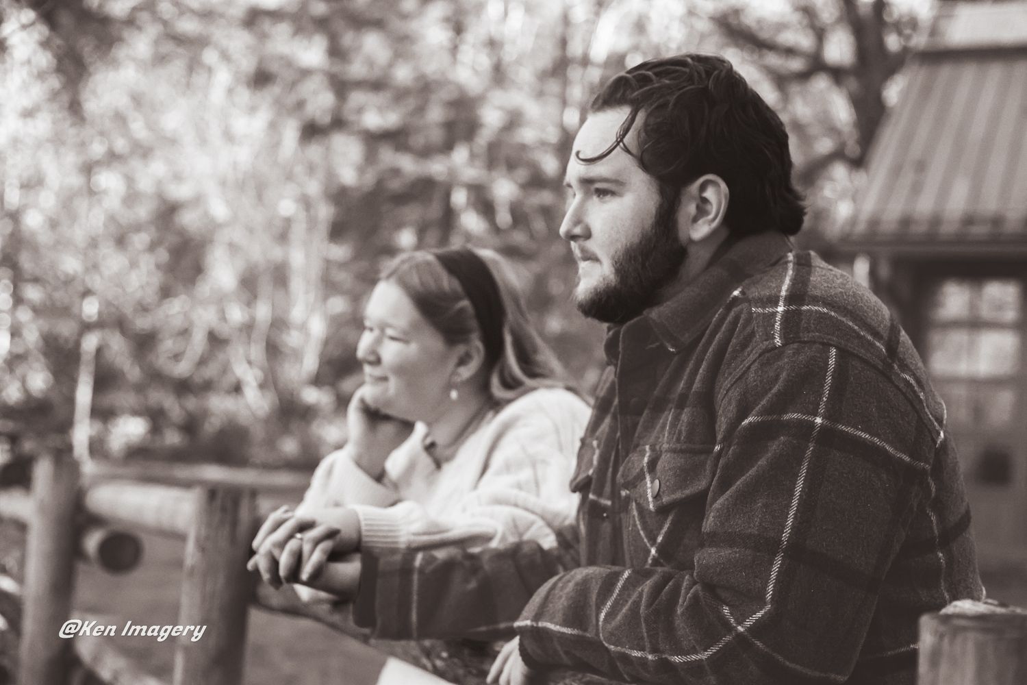 Black and white photo of a man and woman leaning on a fence outdoors, captured in a candid moment.