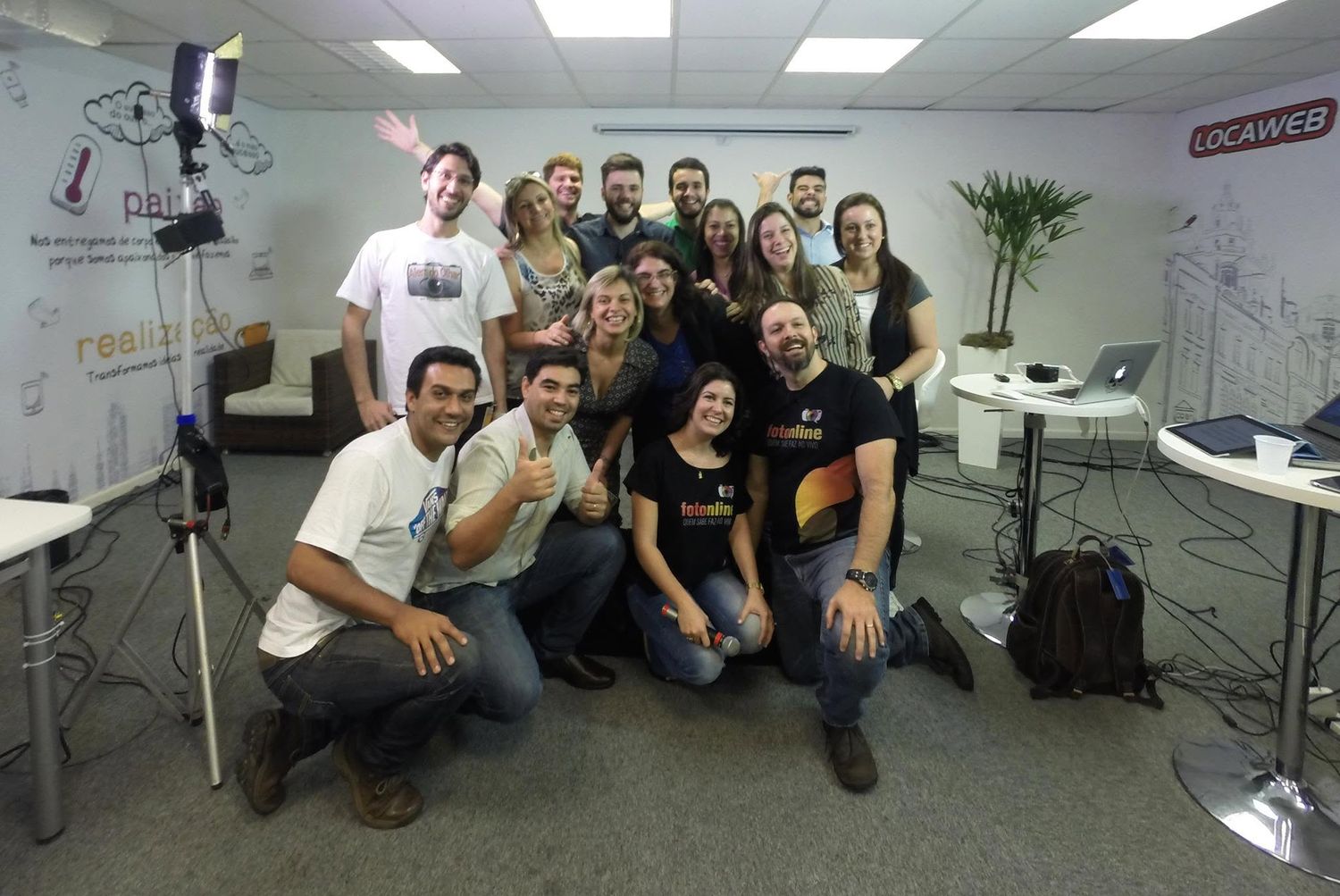 A group of smiling young professionals posing together in a modern office with colorful walls and studio lighting.