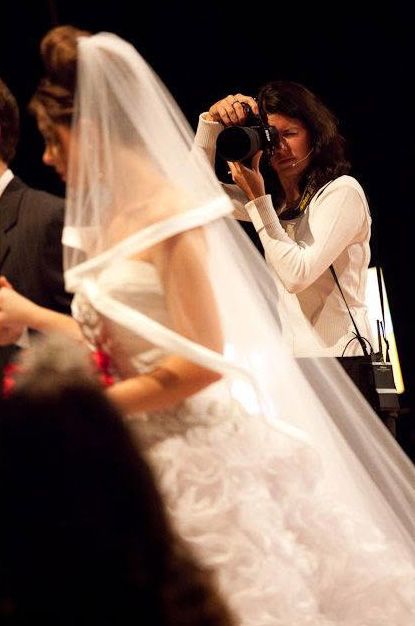 A wedding photographer captures a bride in a white gown and veil during a ceremony.