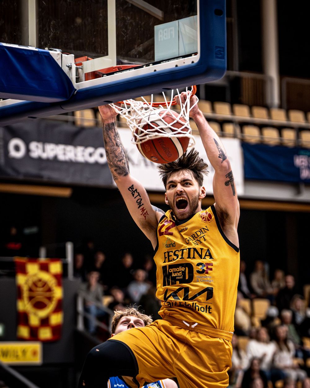 Basketball player in yellow jersey dunks ball through hoop with intensity during a professional league game.
