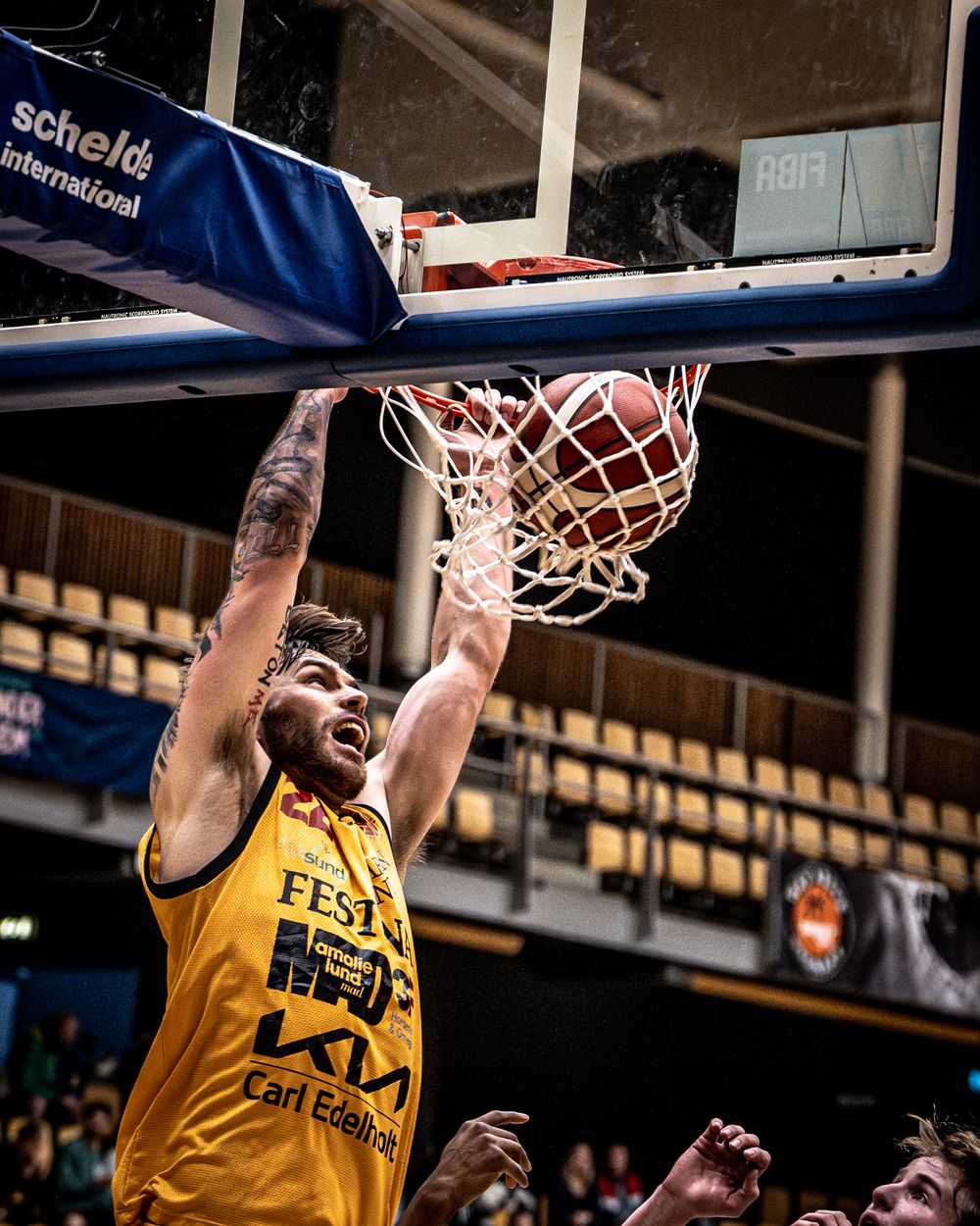 Basketball player in yellow jersey dunks the ball aggressively during a professional indoor game.
