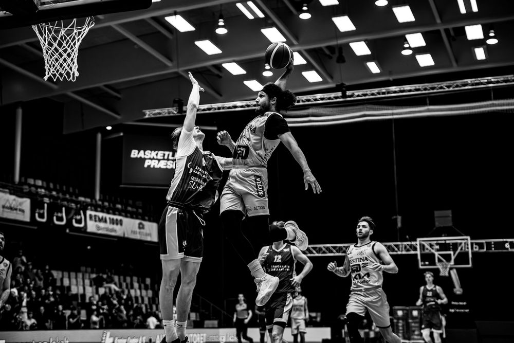 Black and white photo of basketball players jumping for the ball near the hoop during an intense indoor game.