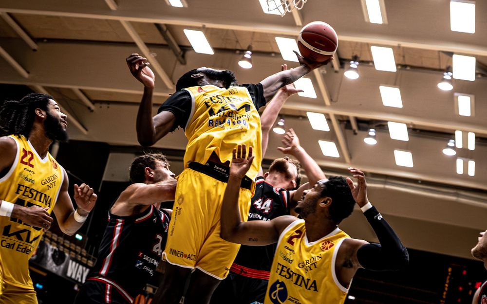 Basketball players in yellow jerseys compete for a rebound during an intense indoor basketball game.