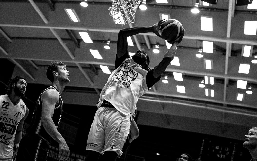 Black and white photo of a basketball player dunking during a game while teammates and opponents watch.