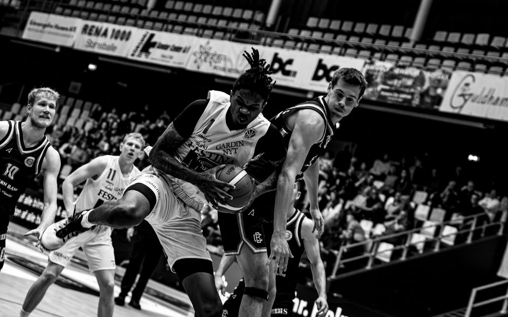 Black and white basketball game action shot with players competing for the ball in an indoor arena.