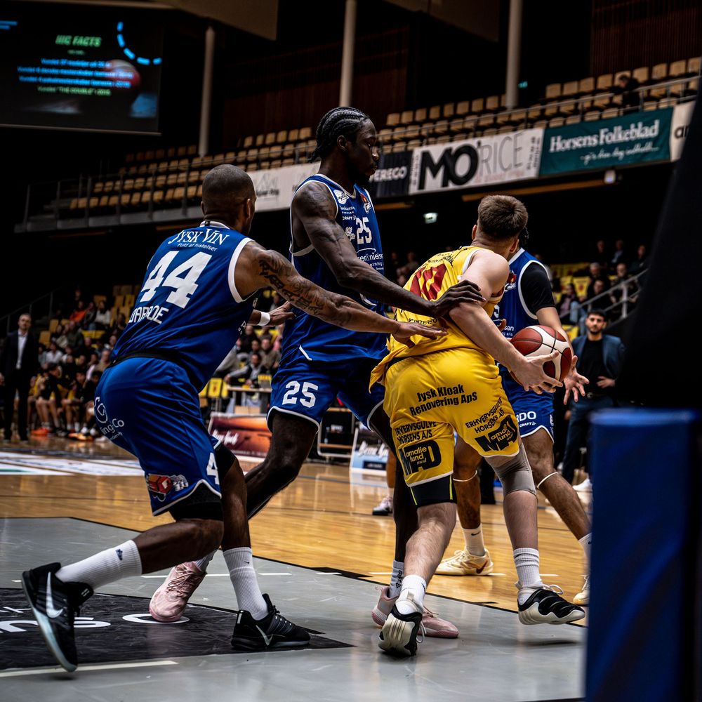Basketball players in blue and yellow jerseys compete intensely on an indoor court during a professional game.