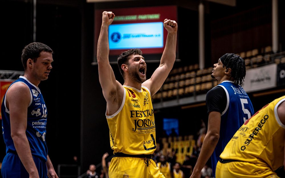 Basketball player in yellow jersey celebrates victory on court, raising fists in triumph during competitive game.