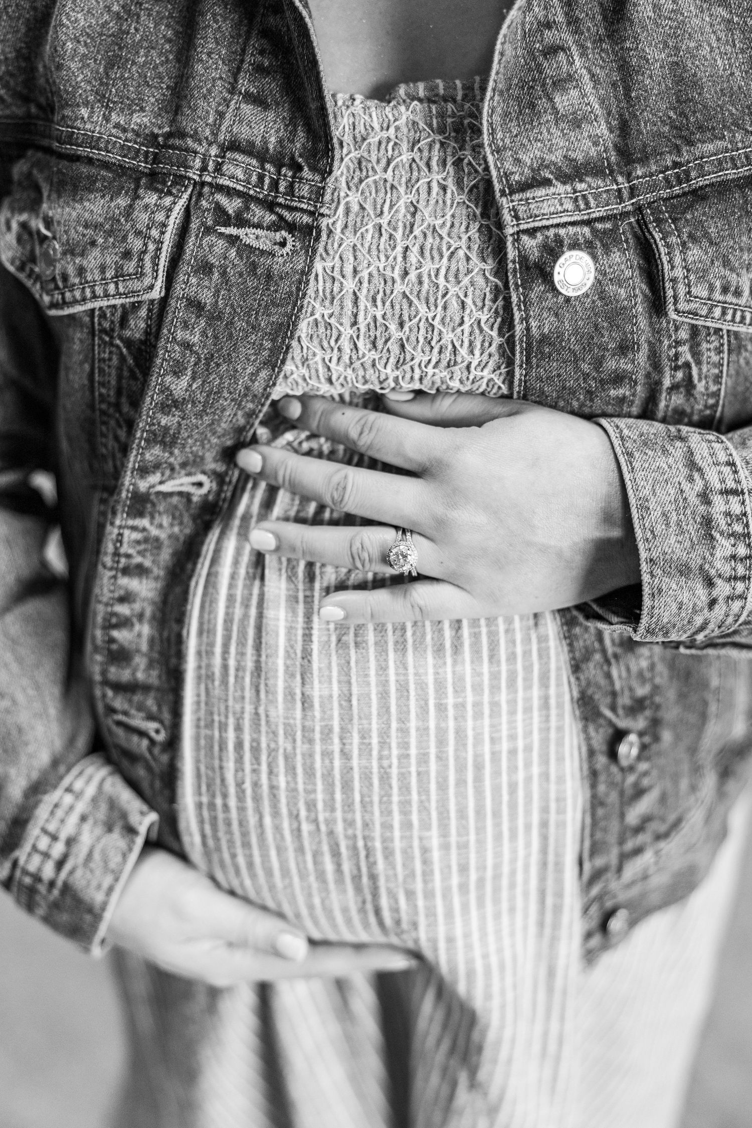 Black and white photo of a pregnant woman cradling her baby bump, wearing a denim jacket and striped skirt.