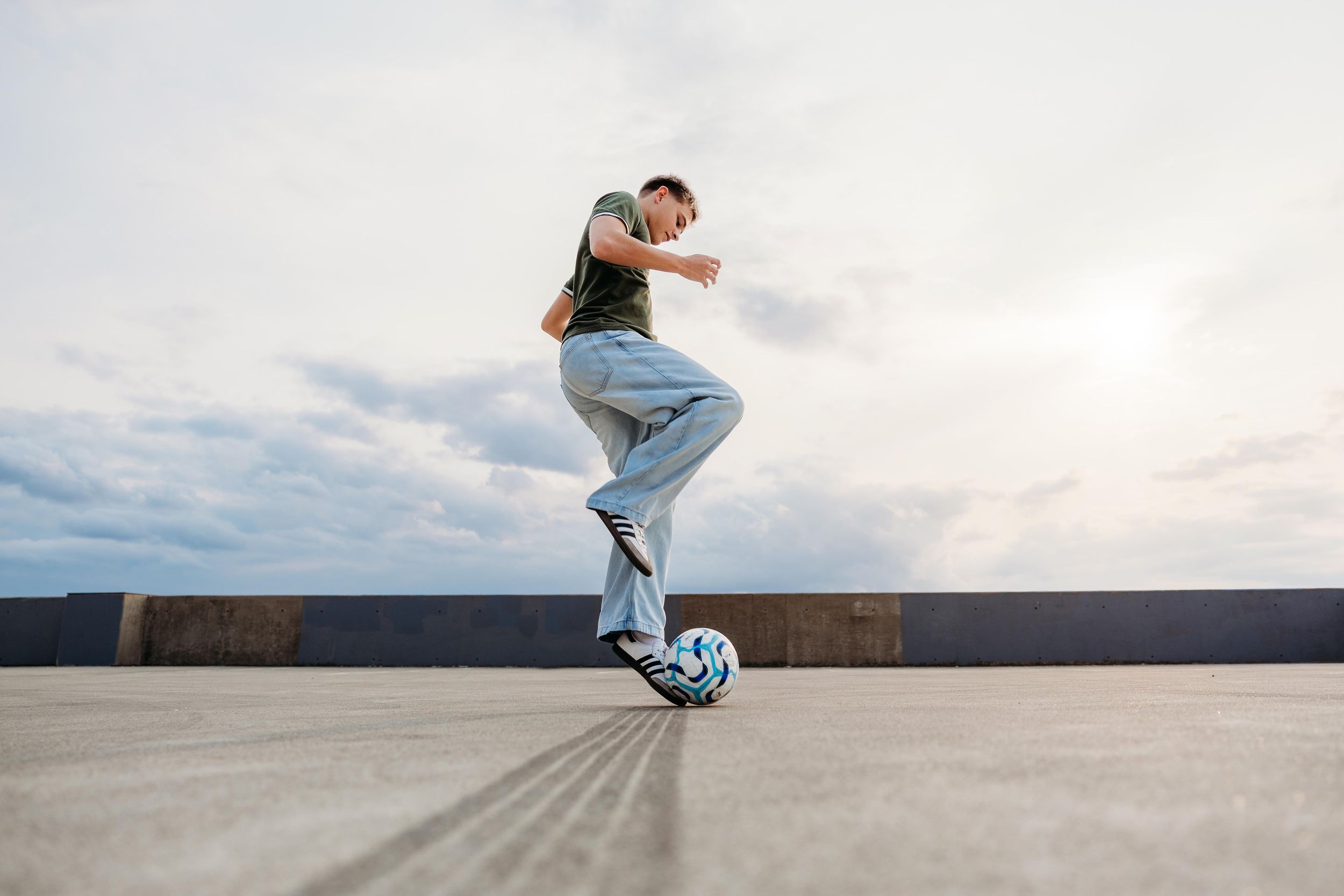 Freestyle footballer balancing a soccer ball under his foot on an outdoor concrete ledge.