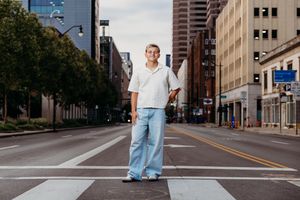 Young person in white shirt and light jeans stands confidently on urban crosswalk in empty city street.