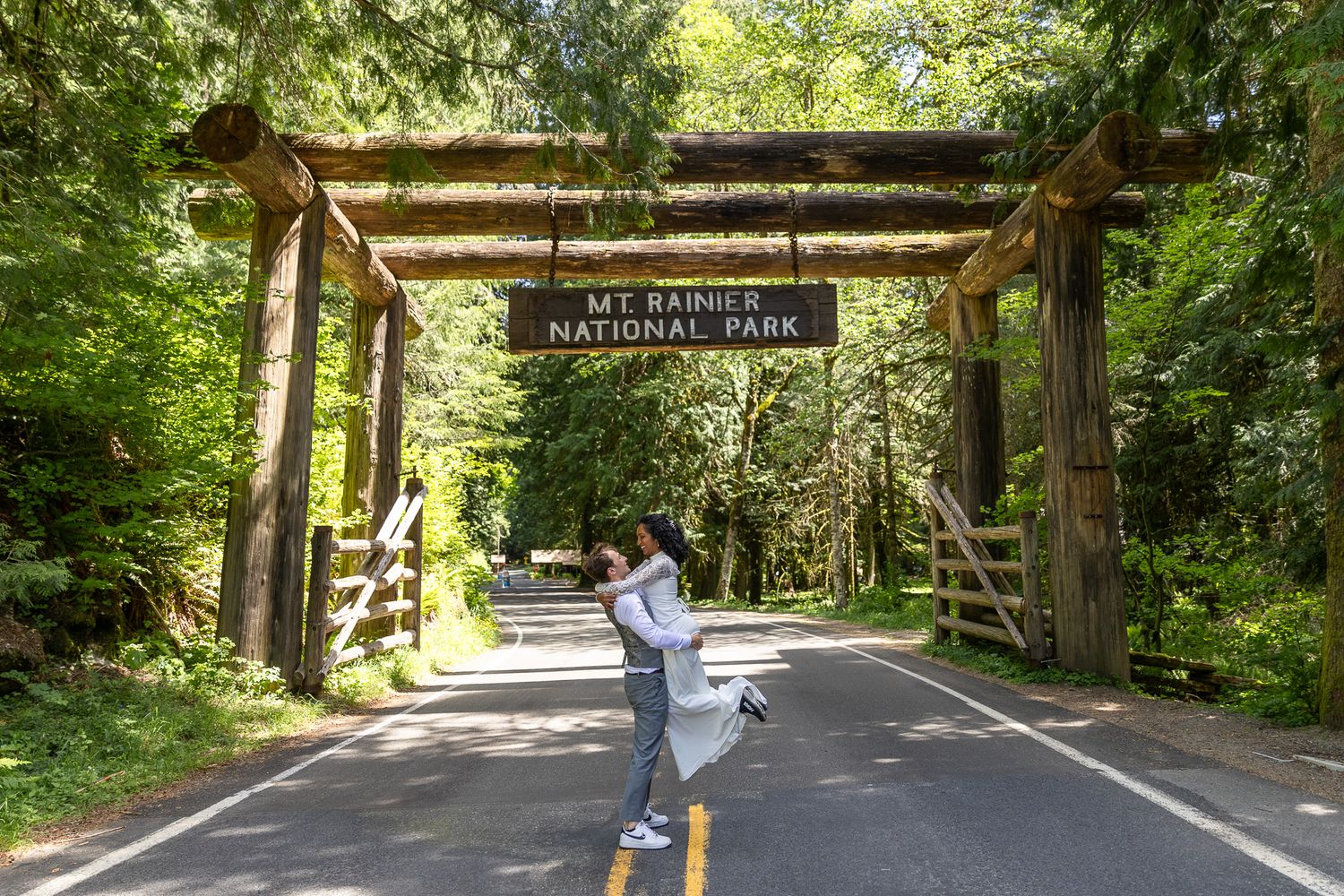 Couple embracing under the Mt. Rainier National Park entrance sign on a forest road. PNW Elopement Photographer