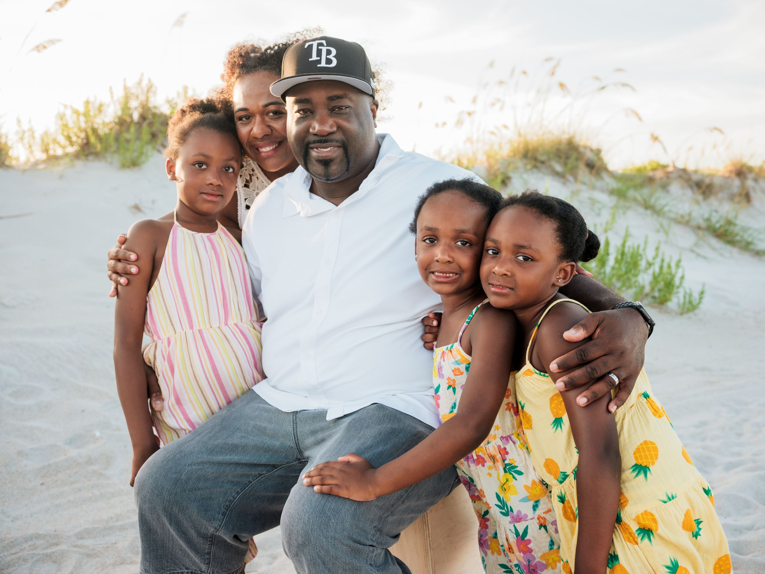 Happy family of five posing together on a sandy beach with sea oats in the background.