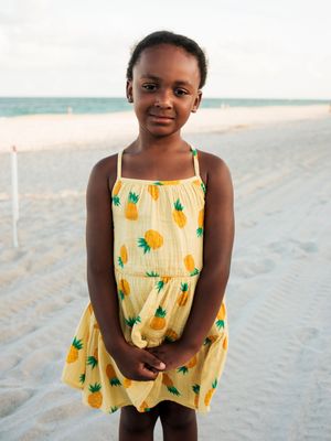 Young girl in yellow pineapple print sundress smiling on a sandy beach.