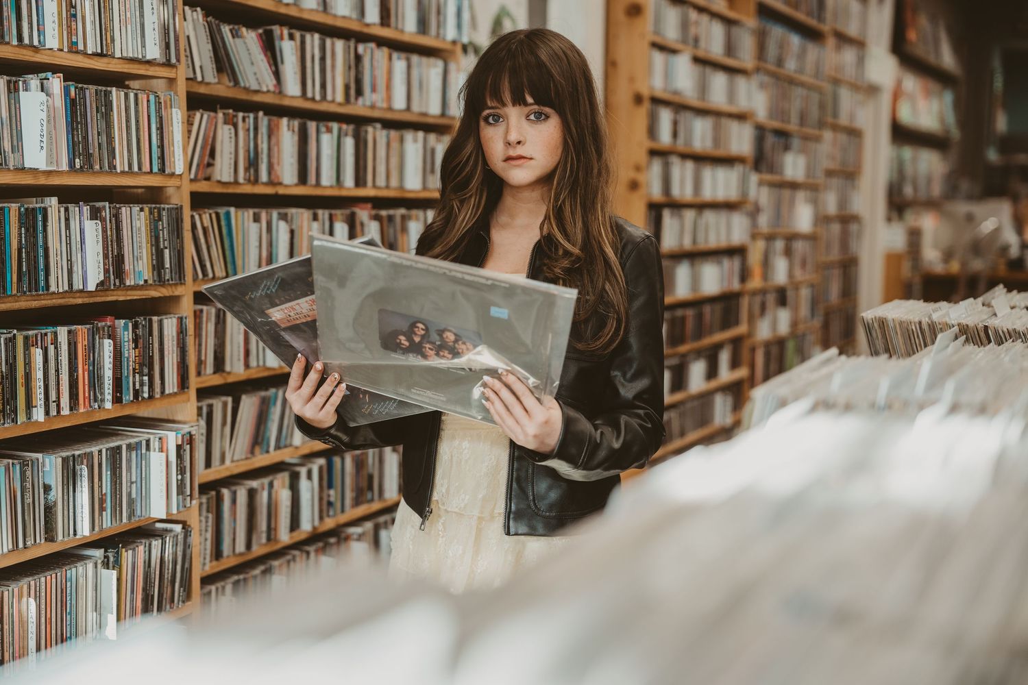 Young woman browsing vinyl records in a music store, holding an album cover among shelves of CDs.