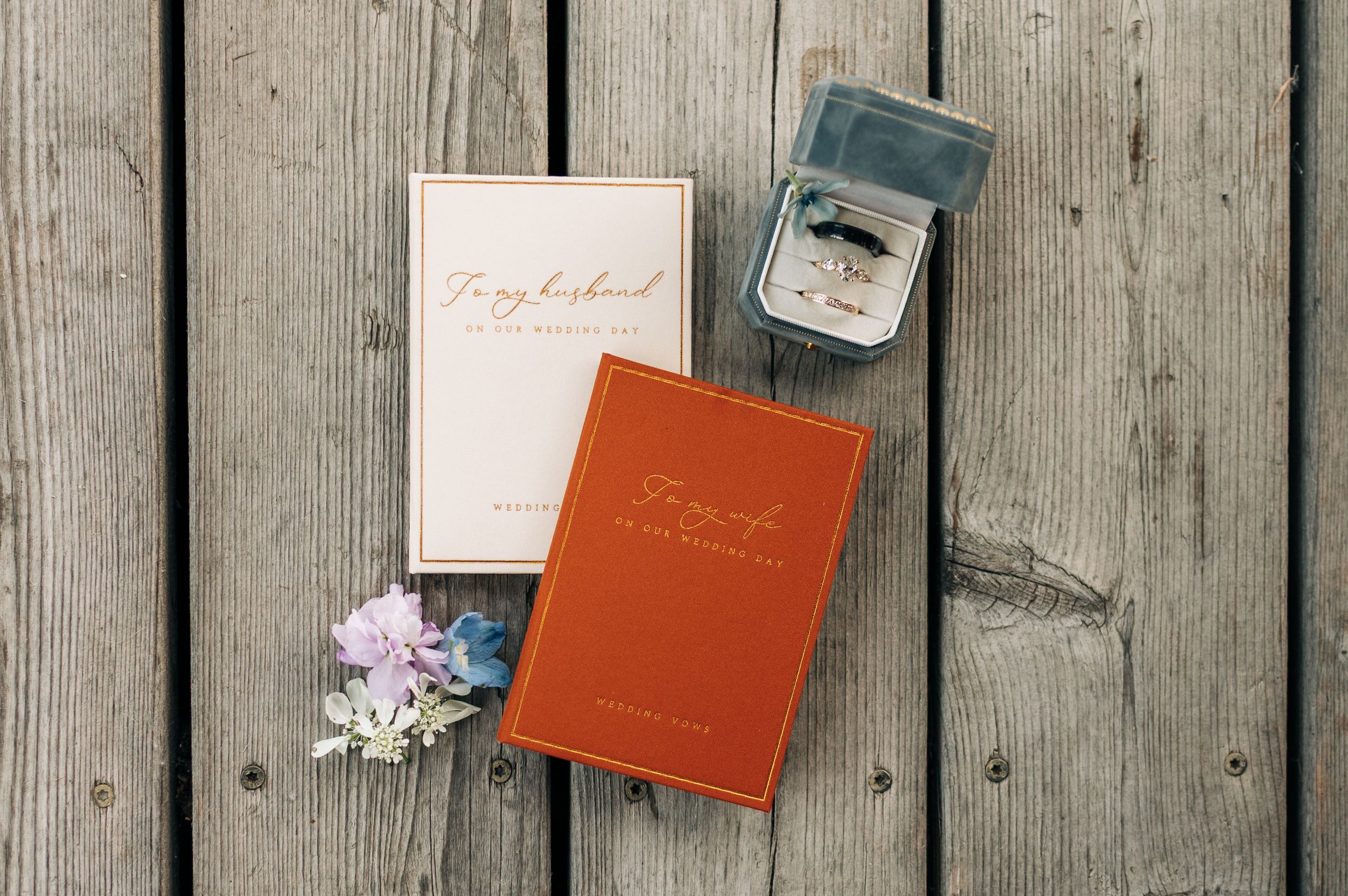 Two elegant books and a ring box with flowers on rustic wood, perfect for a romantic wedding flat lay.