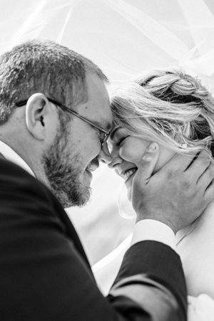 Black and white photo of a laughing bride and groom touching foreheads, the groom tenderly cupping her face.