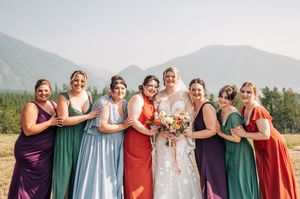 Bride and bridesmaids in colorful dresses pose together outdoors with mountain backdrop on wedding day.