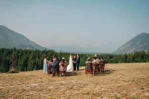 Intimate outdoor wedding ceremony on a mountain meadow with forest and misty peaks in the background.