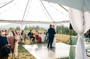 Bride and groom share first dance on white floor under string-lit tent at outdoor mountain wedding reception.