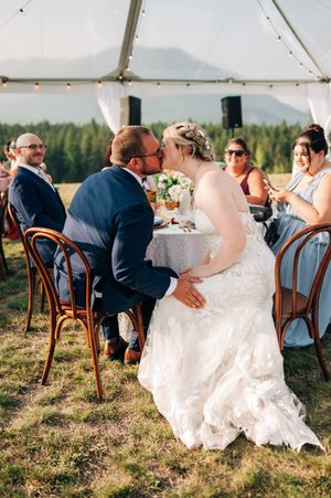 Bride and groom share a kiss at their outdoor wedding reception table with mountain views.