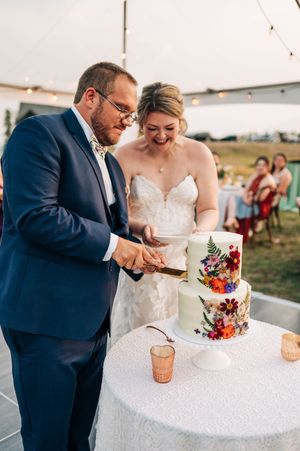 Bride and groom cutting a floral decorated two-tier wedding cake at an outdoor evening reception.