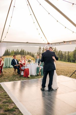 Bride and father share emotional first dance under elegant tent with string lights at outdoor reception.