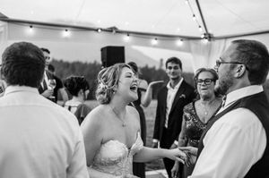 Bride laughing joyfully with guests at an outdoor wedding reception under a tent in black and white.