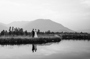 Bride and groom standing by a reflective mountain lake in a stunning black and white wedding portrait.
