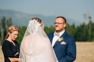 Groom in blue suit gazing at bride during outdoor mountain wedding ceremony on a sunny day.