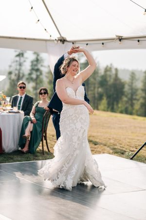 Bride in lace mermaid gown twirls joyfully during first dance at outdoor tented wedding reception.