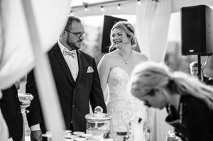 Black and white photo of bride and groom smiling during outdoor wedding ceremony under a tent.