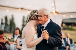 Bride shares an emotional father-daughter dance at outdoor wedding reception under a tent.