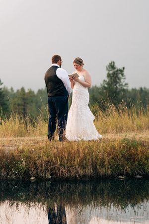 Bride and groom exchange vows outdoors by a reflective pond surrounded by golden meadow grasses.