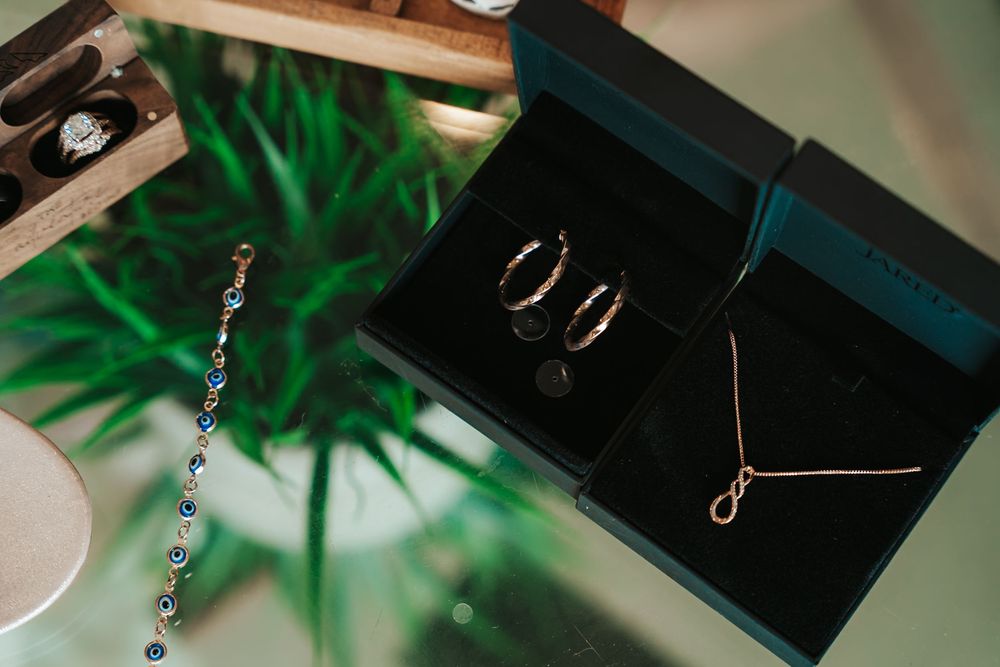 Rose gold necklace and hoop earrings in black jewelry box beside a blue gemstone bracelet on glass table.