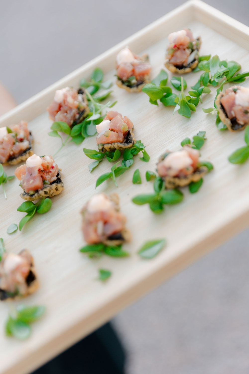 Elegant wooden tray of gourmet salmon tartare appetizers garnished with fresh microgreens at a catered event.