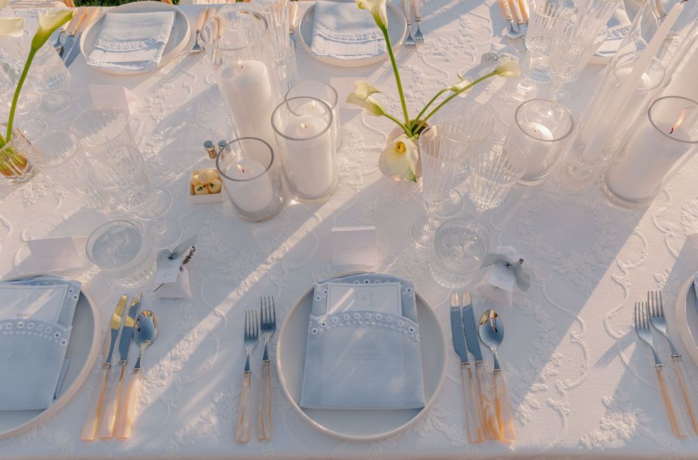 Elegant white wedding table setting with blue napkins, crystal glasses, candles, and floral centerpieces.