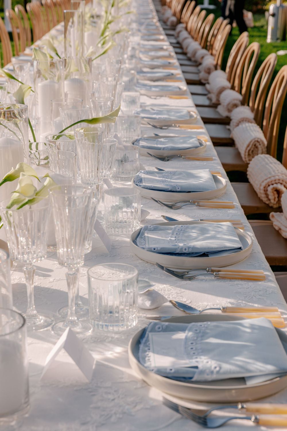 Elegant outdoor banquet table set with blue napkins, crystal glasses, gold cutlery, and white floral arrangements.