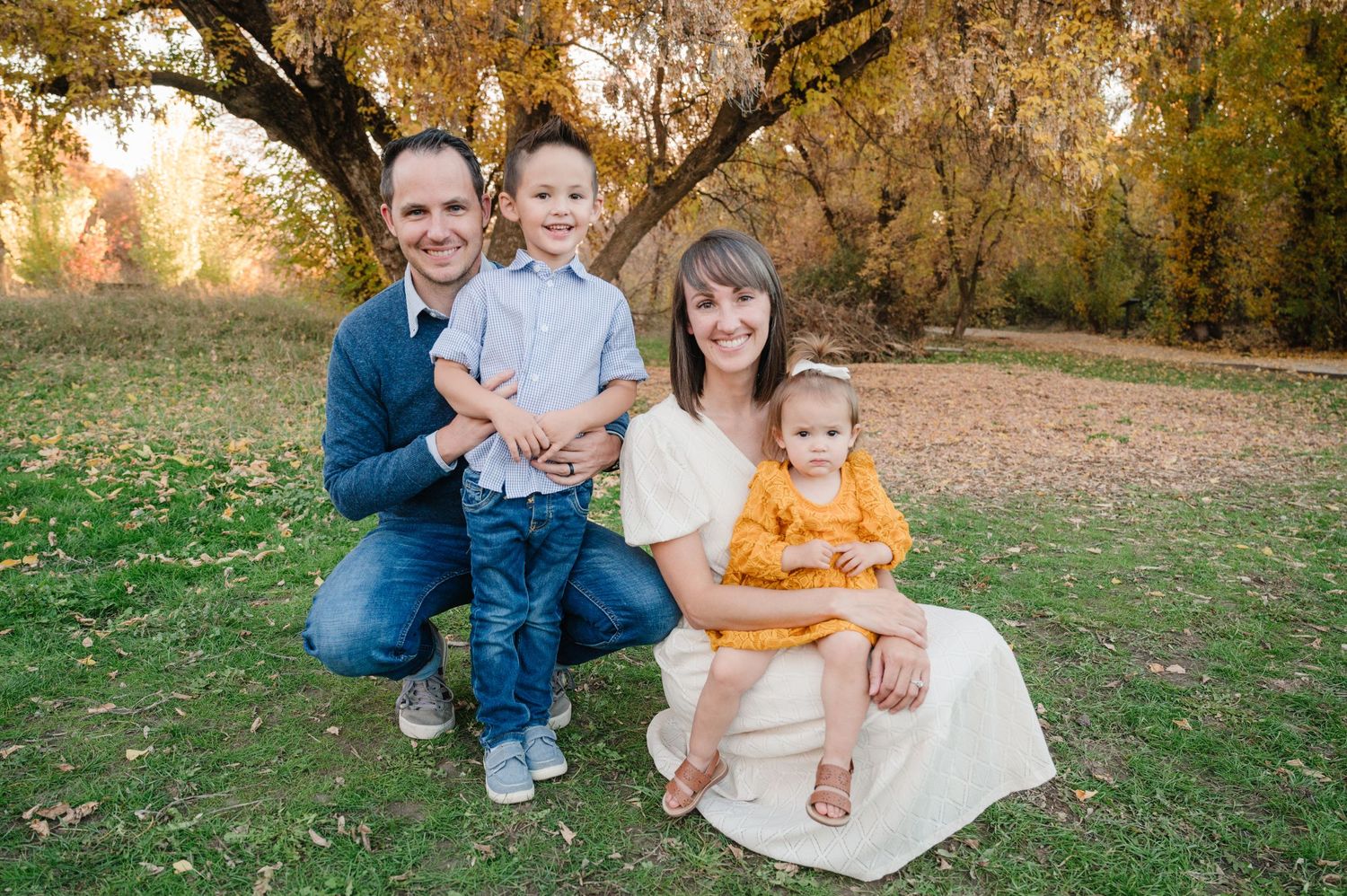 Fall family portrait with autumn trees and warm colors in the background.